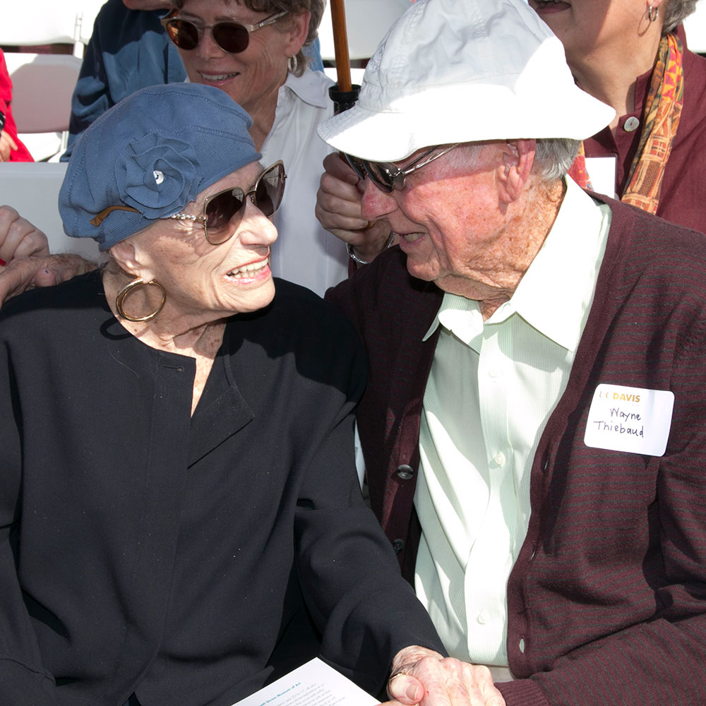 Older woman and man seated, holding hands.