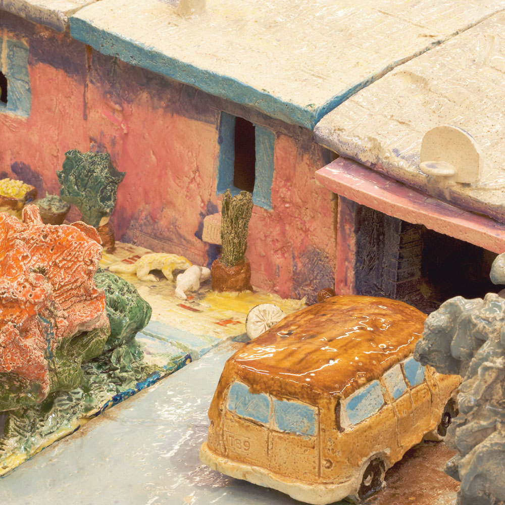 Detail photo of ceramic house showing garage with tan van parked in the driveway and ceramic plants.