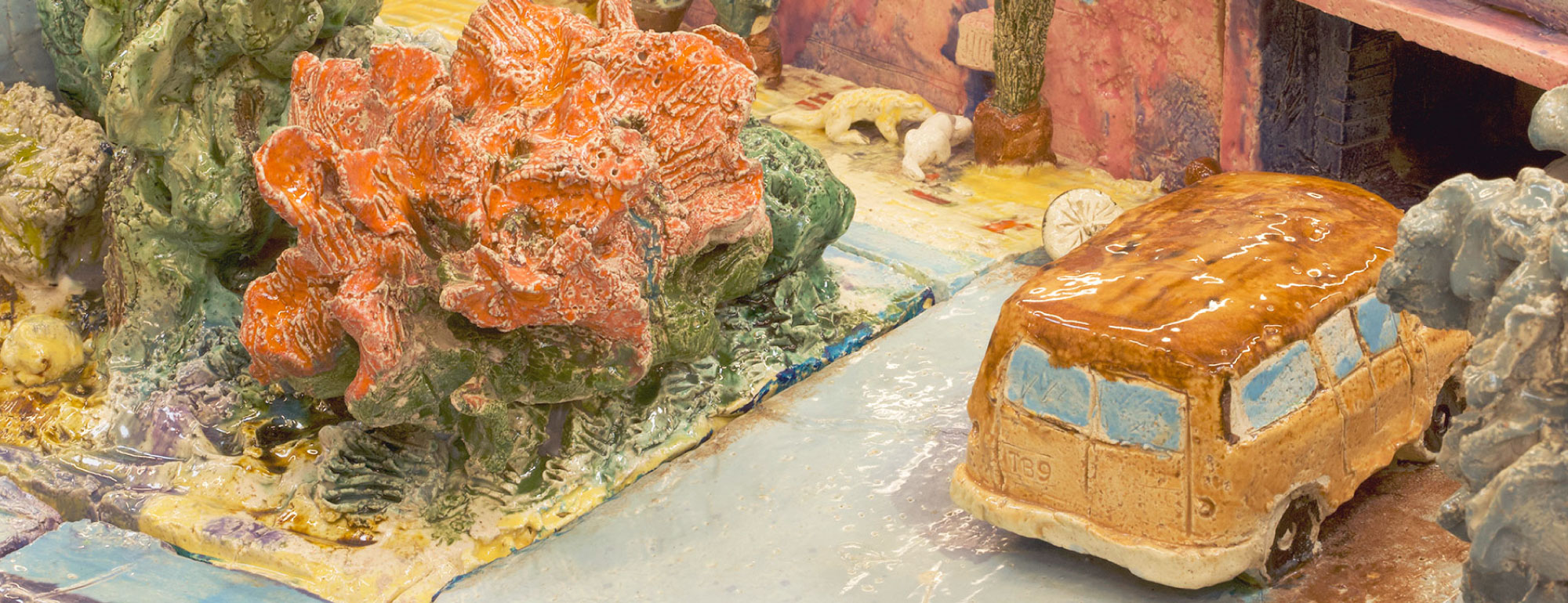Detail of ceramic sculpture of a house showing the garage with a tan van parked in the driveway.