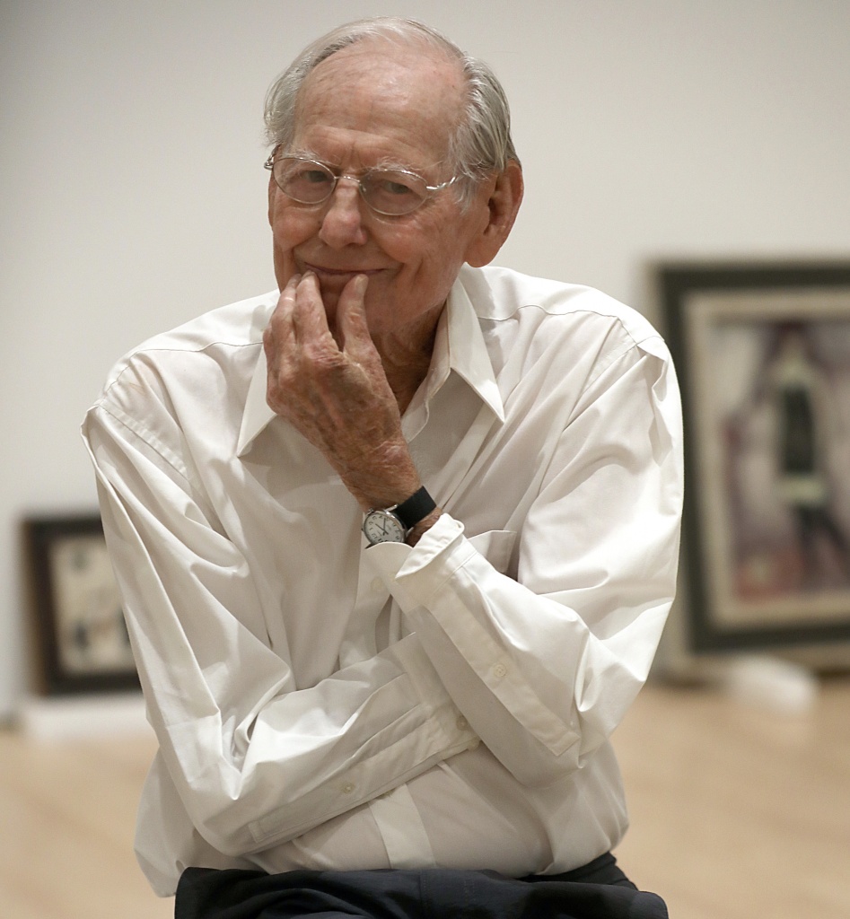 Photo of artist Wayne Thiebaud with artwork leaning against a wall in the background.