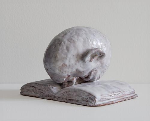 Ceramic maquette of an egghead with it's face in an open book.