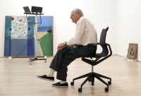 Wayne Thiebaud sitting in a chair in front of some paintings.