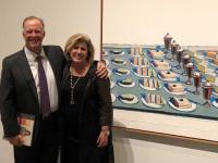 Jeff and Kellie Hepper standing in front of a Thiebaud painting of cakes and pies in the museum gallery.