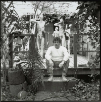 Black and white photo of Manuel Neri sitting in front of his sculptures.