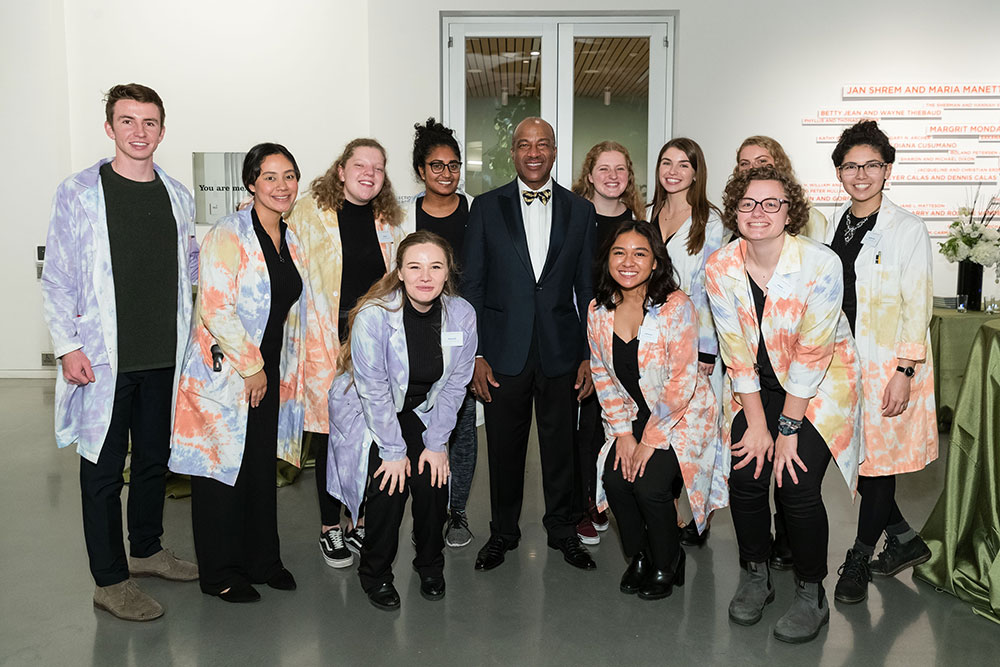 Students in lab coats around the chancellor in the lobby of the museum.