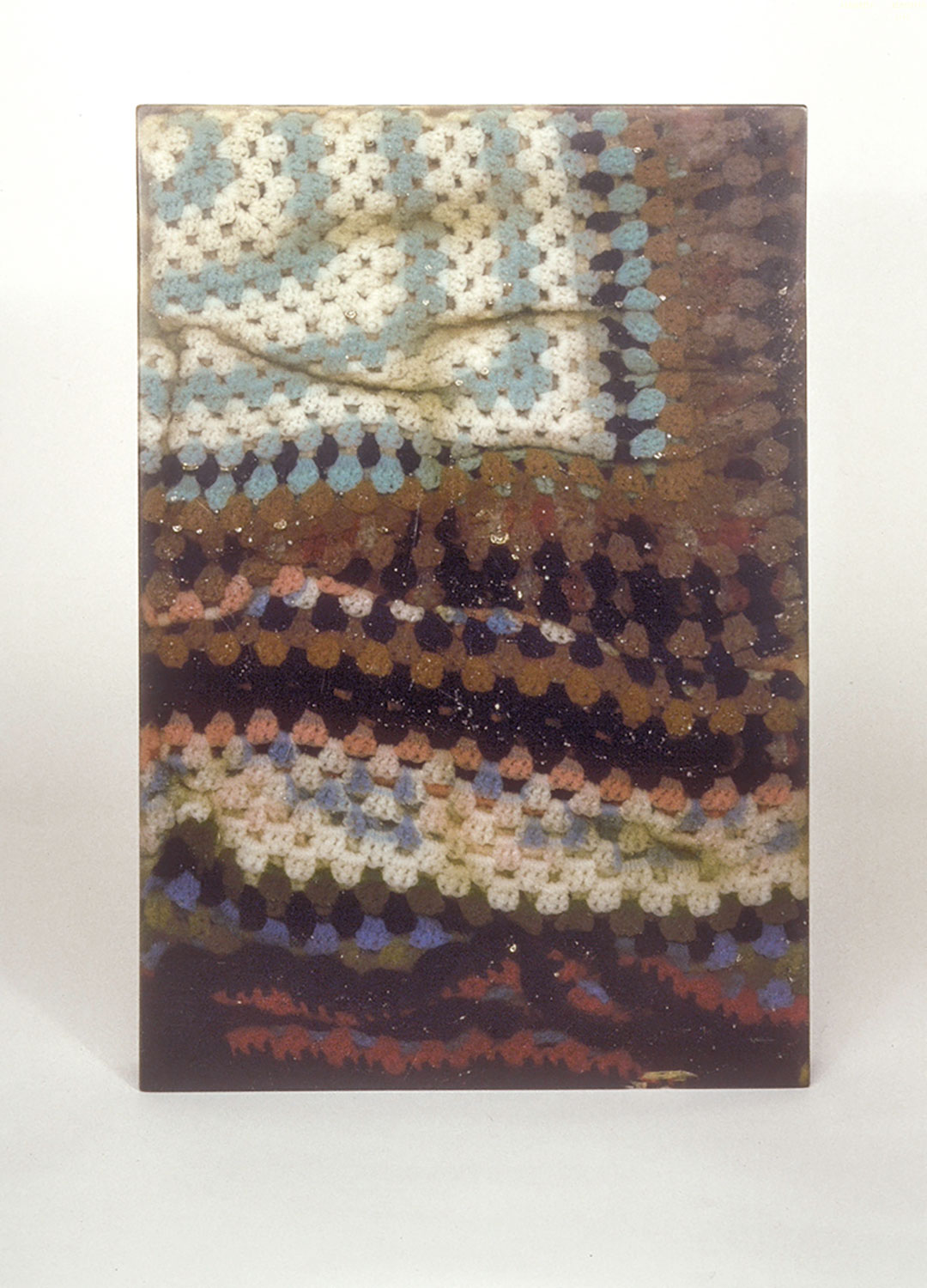 Brown crocheted blanket with blue, cream and darker brown patterns in a resin rectangle.