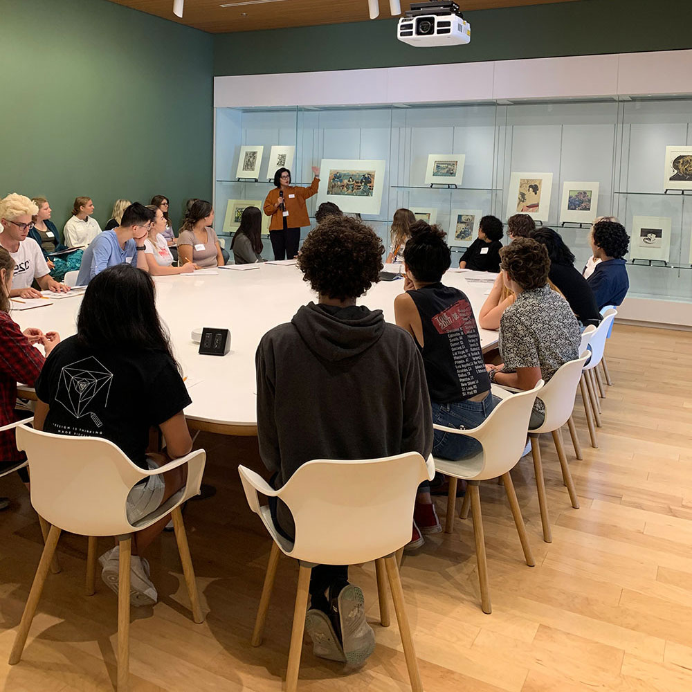 Students in a class sitting around a large white table in a green walled room.