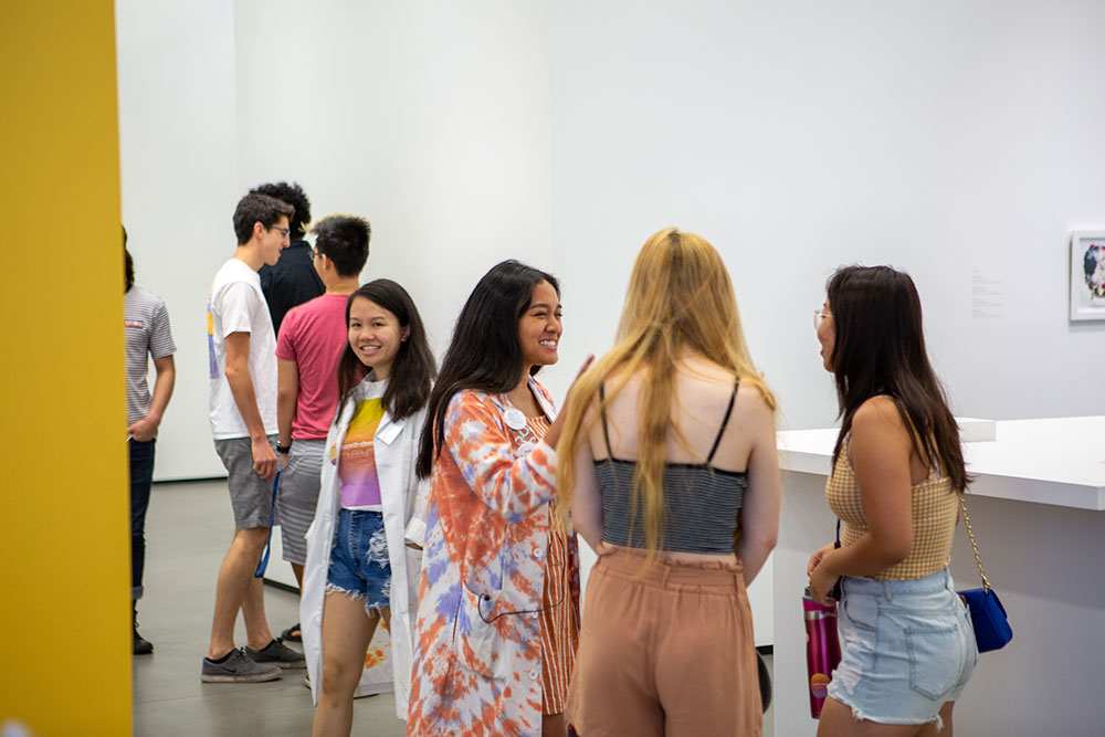 Students talking with another student wearing a tie-dyed lab coat in the museum gallery.