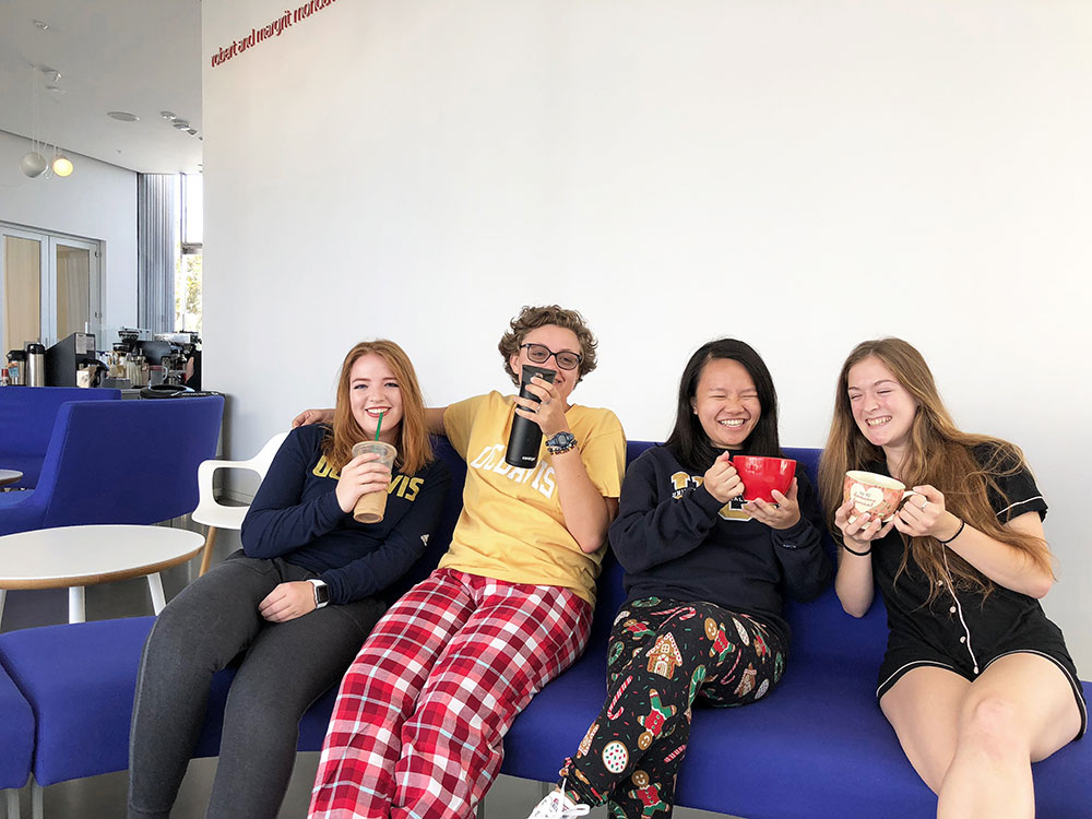 Four students smiling while sitting on a blue couch holding mugs.