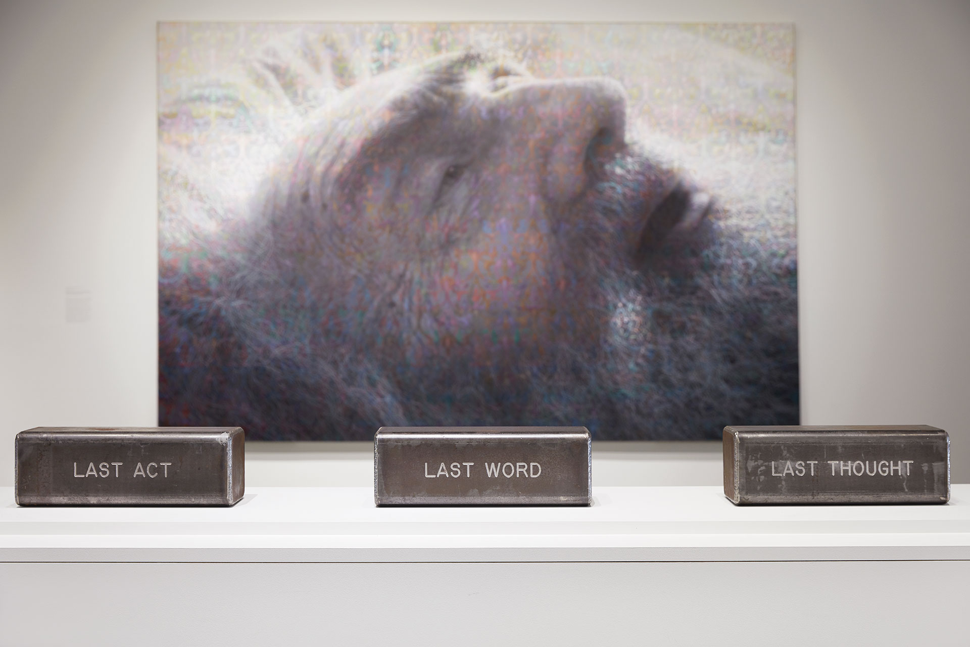 Metal boxes with the words 'last act', 'last word' and 'last thought' on them in front of a painting of an elderly man.