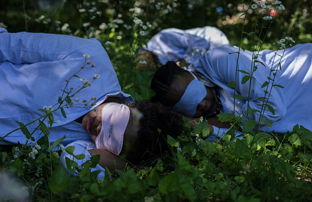 Three people with eye masks on and blue shirts sleeping among plants.