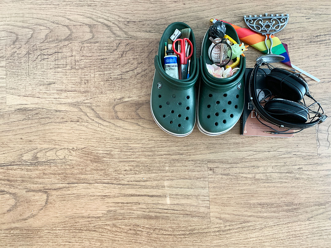 Various found objects like shoes, headphones, flag, shells and art supplies on a wooden table.