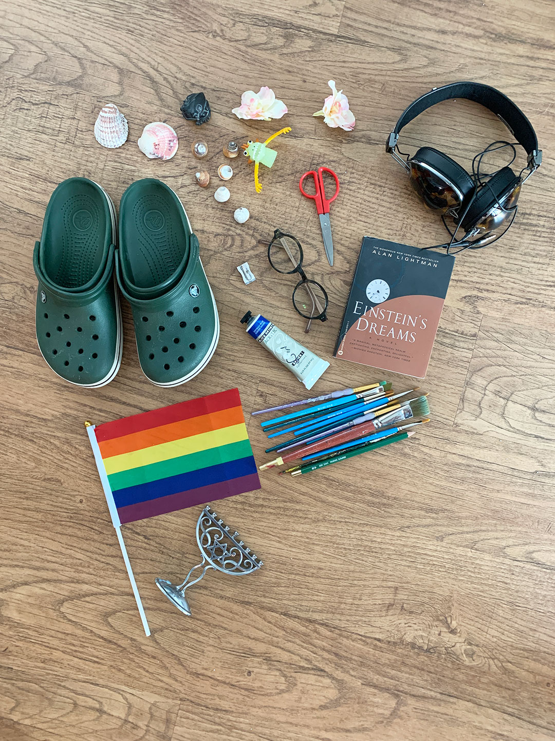 Various found objects like shoes, headphones, flag, shells and art supplies on a wooden table.