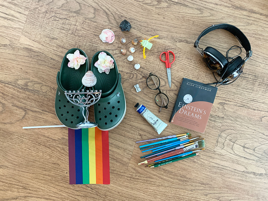 Various found objects like shoes, headphones, flag, shells and art supplies on a wooden table.