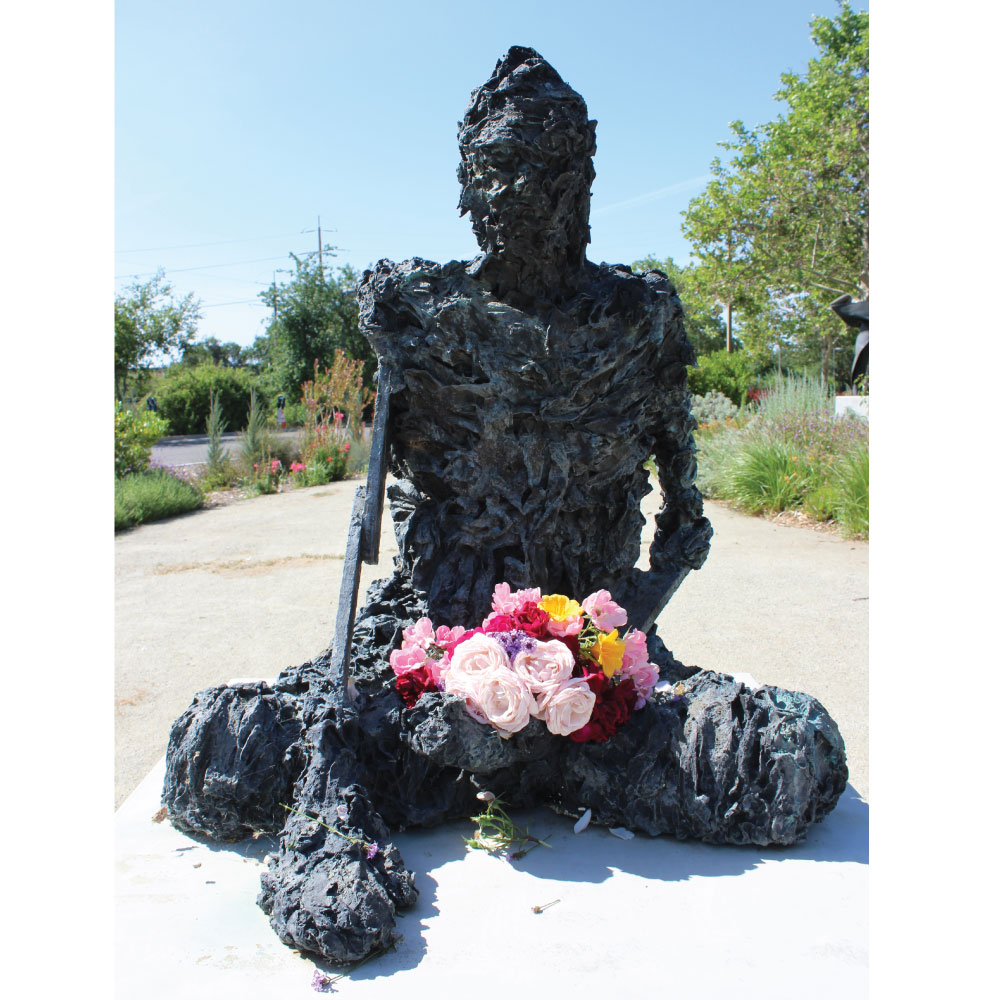 Sculpture of modern style Buddha sitting on a concrete platform with a hand reaching down to touch it.