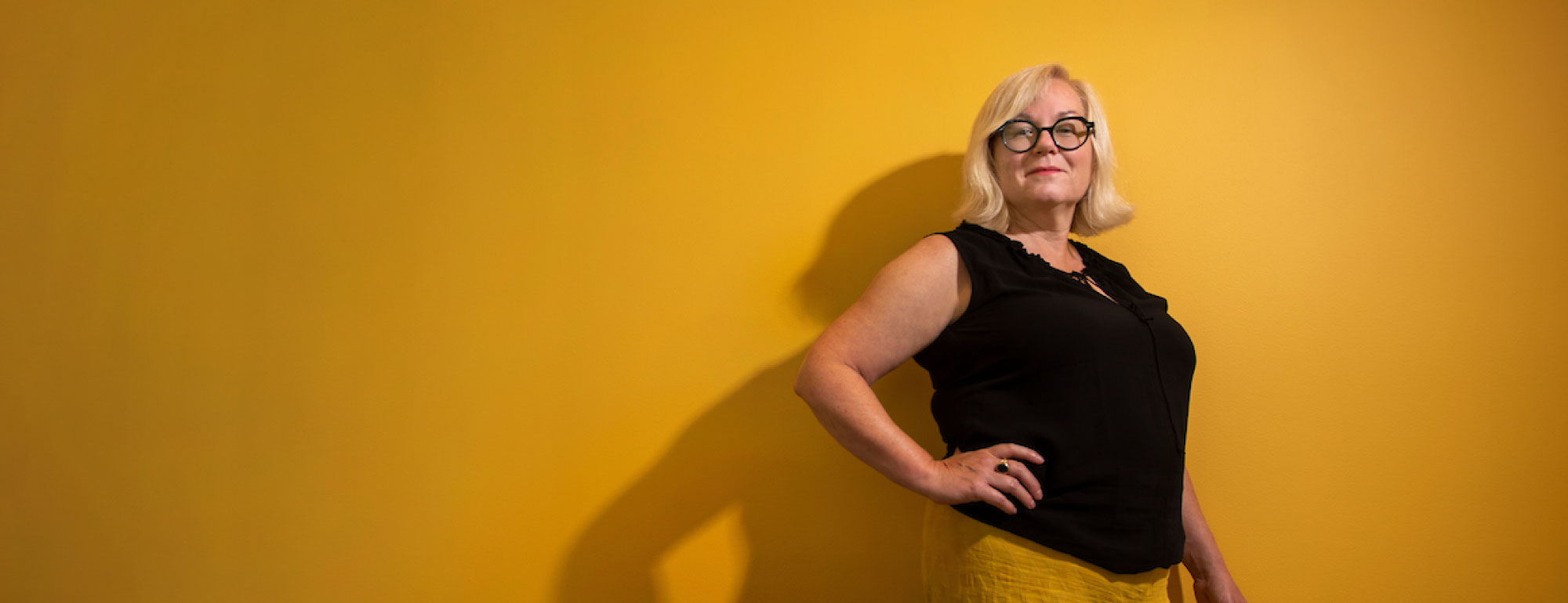 Woman in front of bright yellow wall.