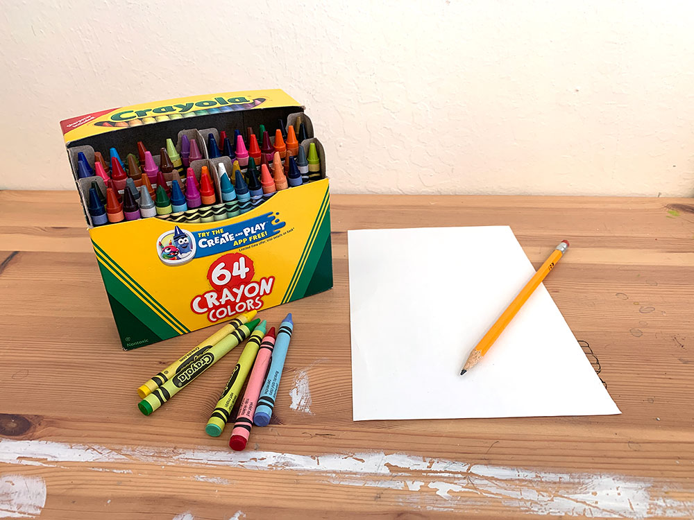 Box of crayons, blank paper and pencil on wooden table.