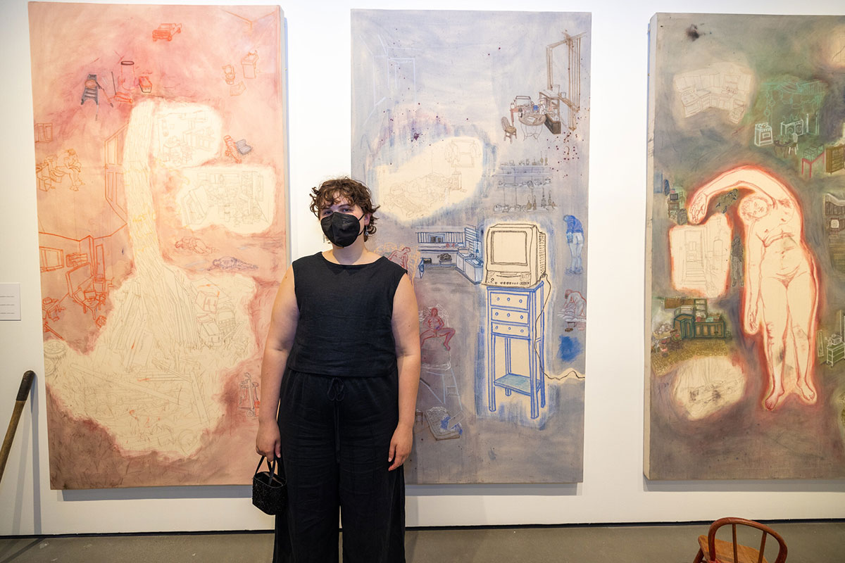 Artist Gracieanne Kirsch standing in front of their artwork on three canvases..