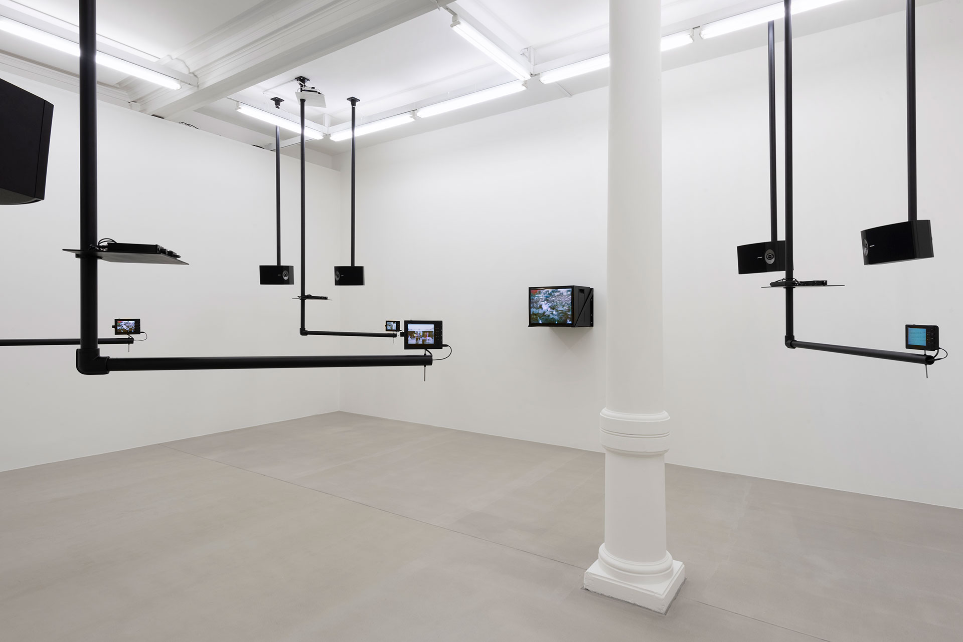 Installation view of video piece by Dara Birnbaum showing various monitors suspended from the ceiling via black pipes.