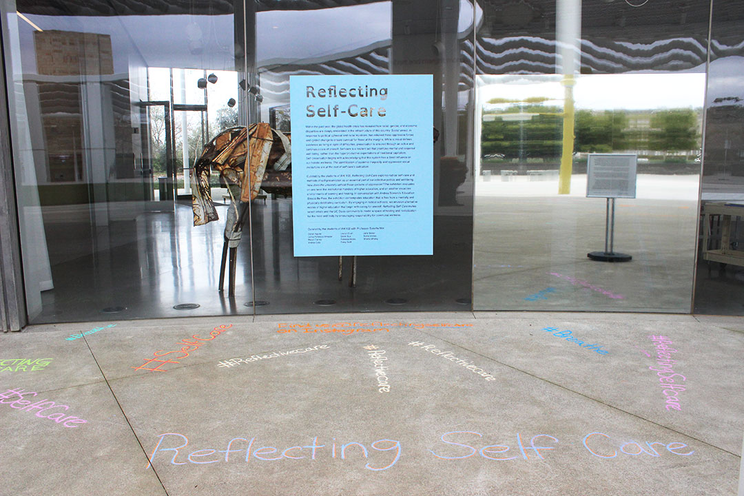 Front of the museum with a blue vinyl informational piece saying 'Reflecting Self-Care' and various phrases in chalk below.