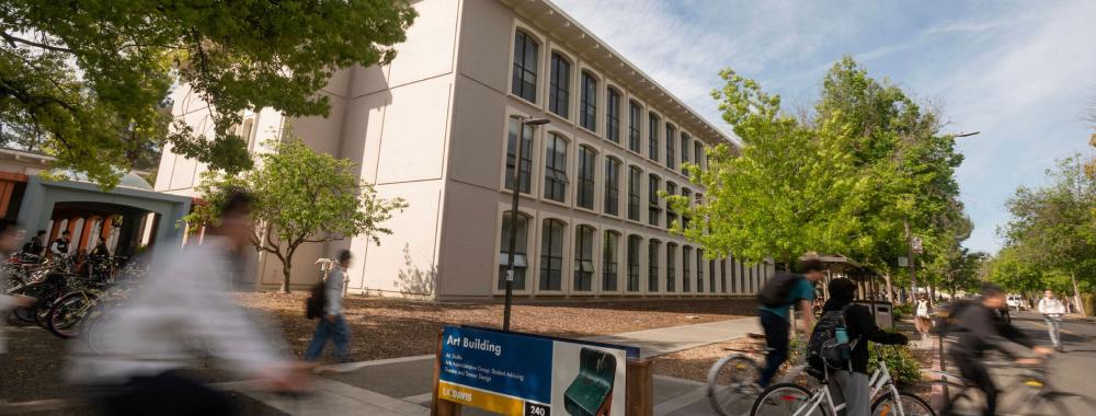 Students on bikes ride past the art building on campus.