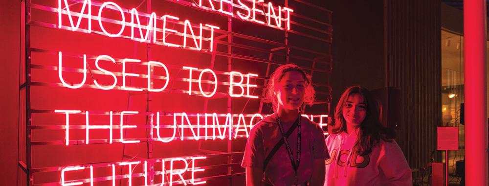 Students standing in front of a neon artwork.