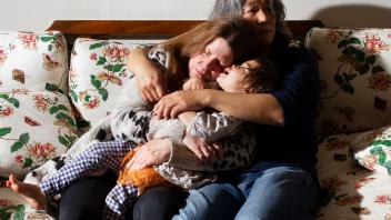 Two people and a child hugging on a couch.