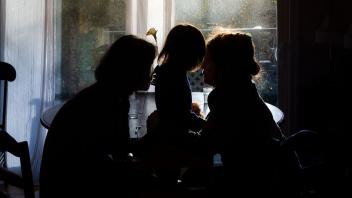 Two people and a child hugging in front of a sunlit window.