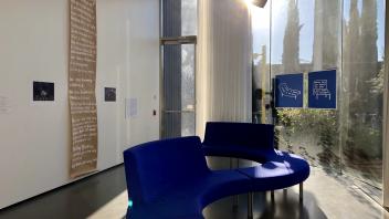 Artwork on the wall and window and a blue winding couch in the museum.