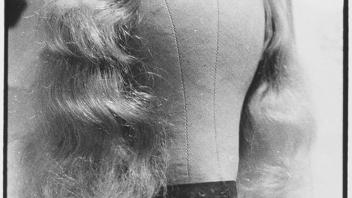 Black and white photo of a blonde wig on a wig stand. 