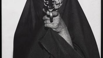 Black and white photo of a woman pointing a gun at the camera with writing painted on her face.