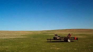 Transplant Module, 2021, 35mm film series. Utility trailer; replica of an NYC park bench; lodgepole pine roots; soil from a construction site; traffic cone; road barrier; survey flags; open prairie.