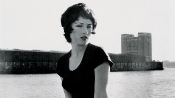 Black and white photo of woman in black short sleeved top looking over her shoulder.