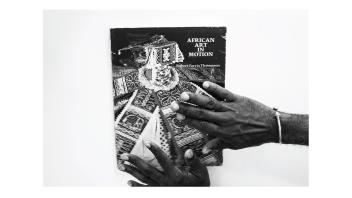 Black and white photo of hands holding a book titled 'African Art in Motion' by Robert Farris Thompson.
