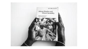 Black and white photo of hands holding a book titled 'African Rhythm and African Sensibility' by John Miller Chernoff.