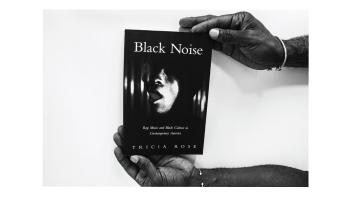Black and white photo of two hands holding a book titled 'Black Noise' by Tricia Rose