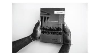 Black and white photo of hands holding a book titled 'Democracy: A Project by Group Material'.