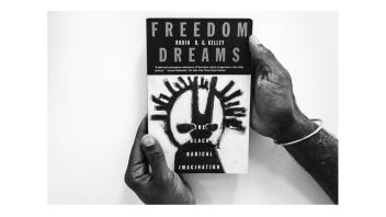 Black and white photo of hands holding a book titled 'Freedom Dreams' by Robin D. G. Kelley.