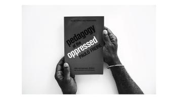 Black and white photo of hands holding a book titled 'Pedagogy of the Oppressed' by Paulo Freire.