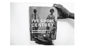 Black and white photo of hands holding a book titled 'The Short Century' by Okwul Enwezor.