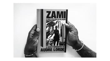 Black and white photo of hands holding a book titled 'Zami, A New Spelling of My Name' by Audre Lorde.
