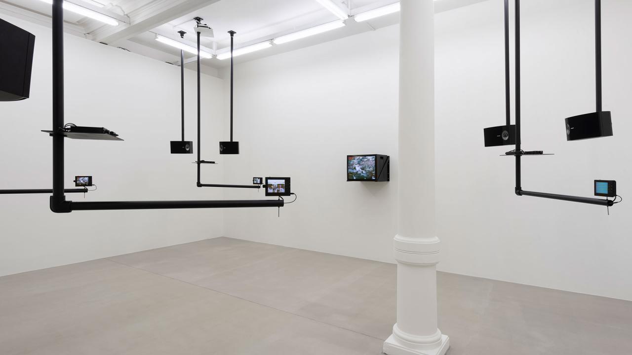 Installation view of video piece by Dara Birnbaum showing various monitors suspended from the ceiling via black pipes.