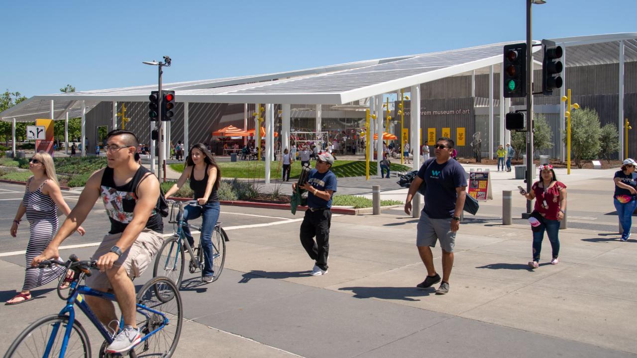 Students crossing the street on foot and on bikes in front of the museum.