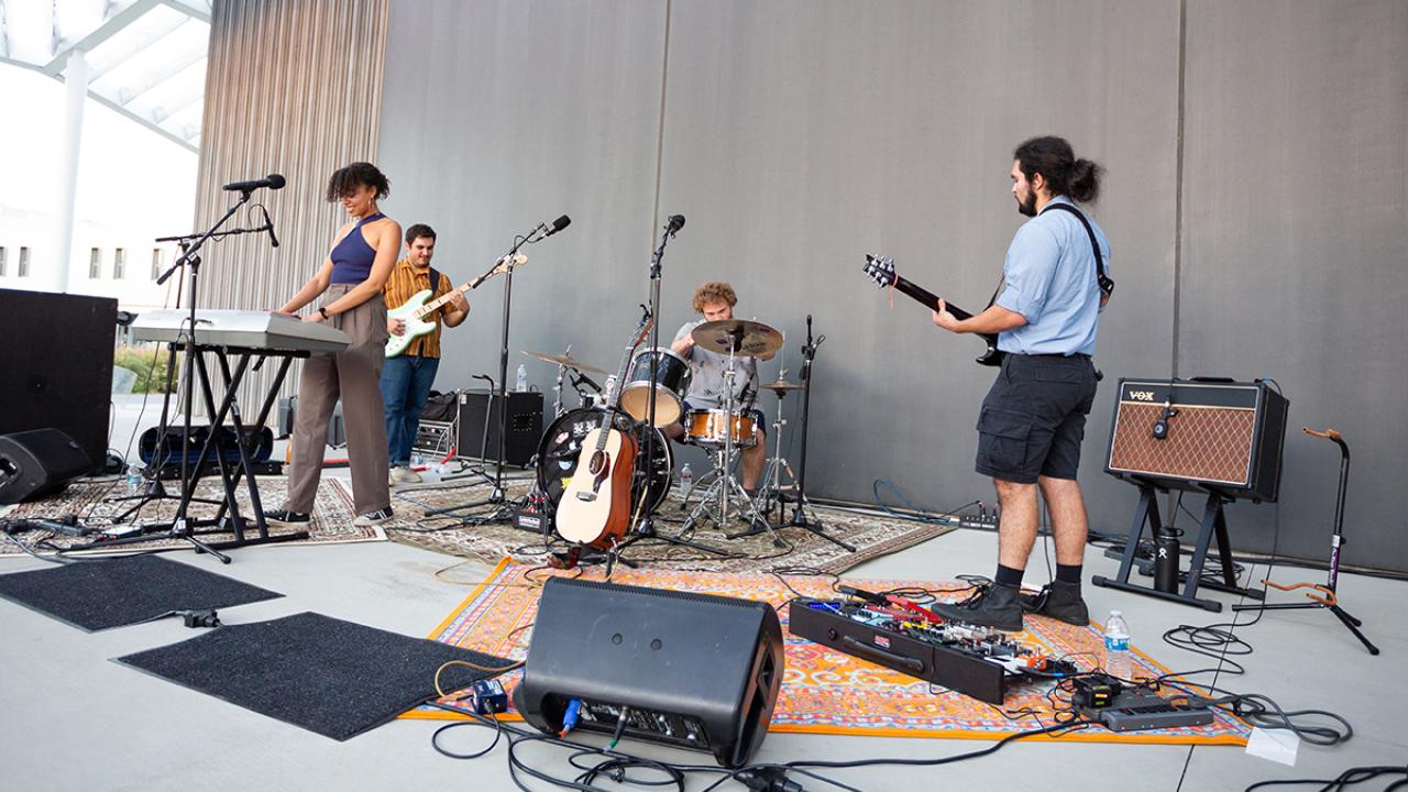 Three musicians rehearsing on stage: keyboardist, drummer, and guitarist