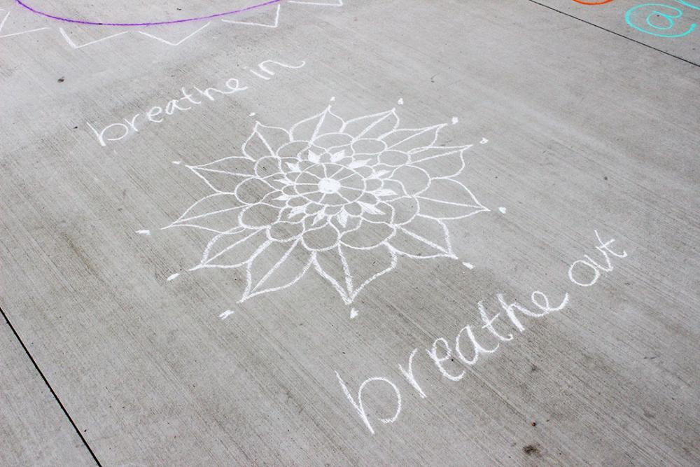 White chalk drawing of a flower and the words 'breathe in, breathe out'.