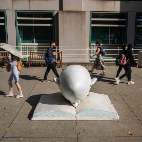Students walking past Bookhead egghead sculpture on campus.