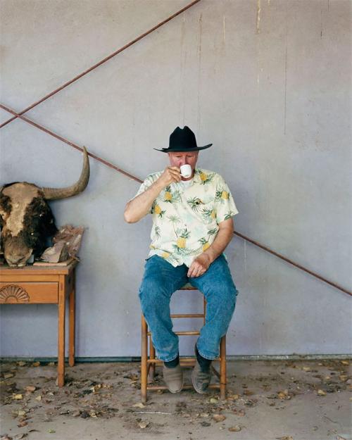 Artist Bruce Nauman wearing cowboy hat sitting on a chair drinking out of a mug.