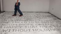 Multiple lines of text written into salt on the floor with a person walking over them in the upper left.