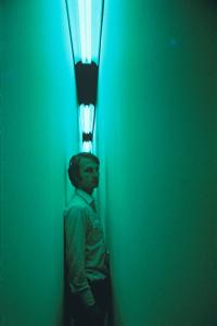 Bruce Nauman in a green lit narrow corridor.
