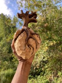 Hand holding a carved wooden heart with trees in the background.